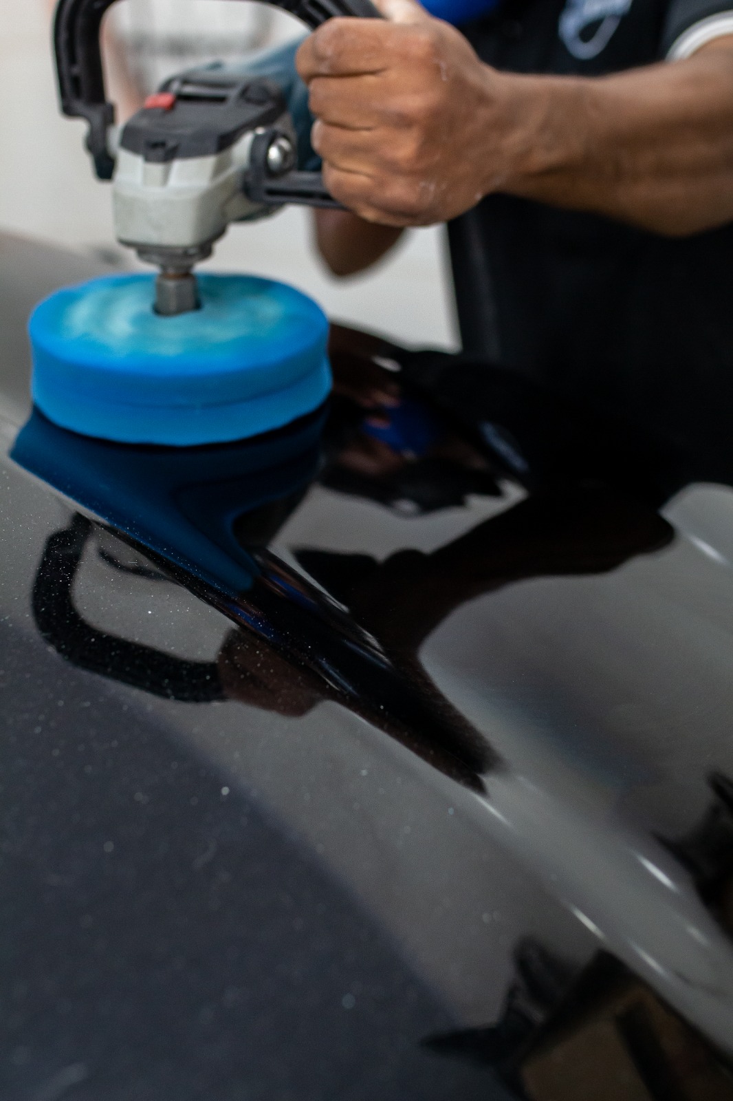 Politriz com boina azul trabalhando o verniz preto de um carro